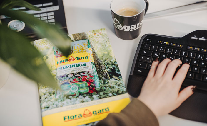 Ein Floraland Katalog auf einem Tisch neben einer Tastatur einem Kaffe und einer Pflanze