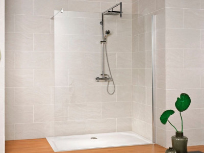 Eine moderne, bodenebene Dusche mit Glasabtrennung und Handbrause ist in eine hell geflieste Badezimmerwand integriert. Am rechten Bildrand steht eine grüne Zimmerpflanze in einer Vase