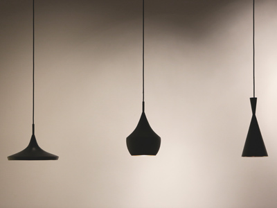 Drei schwarze Hängelampen mit unterschiedlicher Form hängen vor einer neutral beleuchteten Wand.